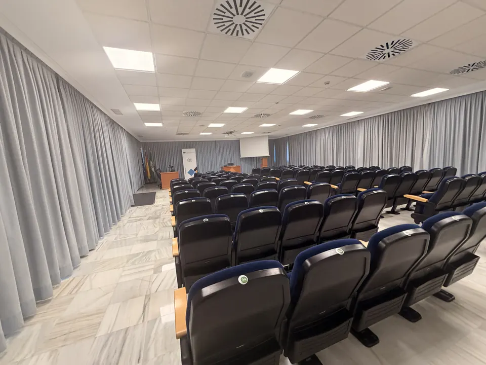 Rows of dark seats in a bright hall with grey curtains